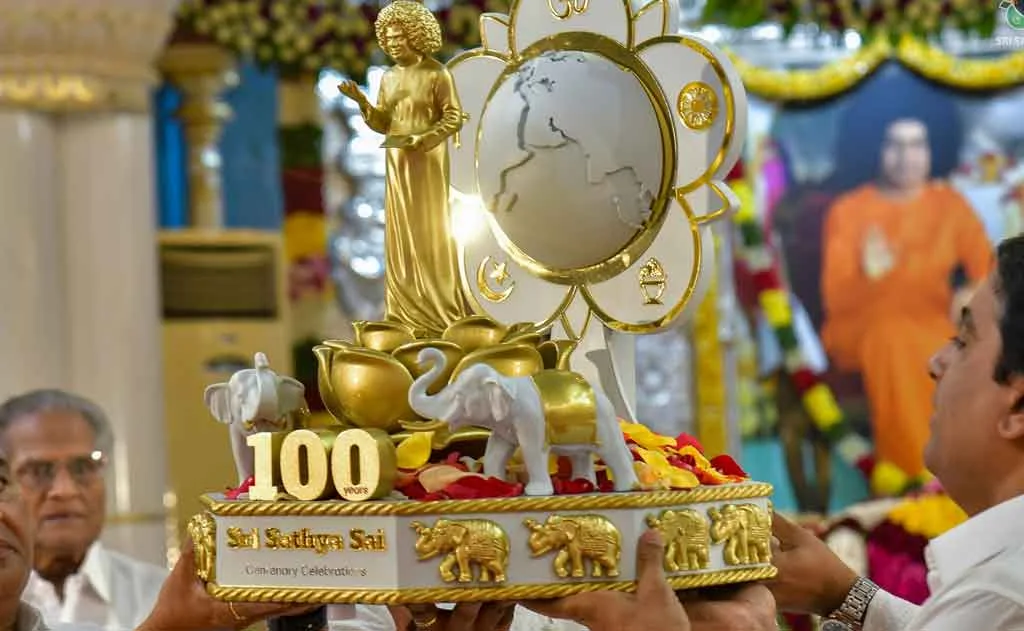 Bhagawan Sri Sathya Sai Baba smiling divinely with golden 100th Birthday logo and Prasanthi Nilayam in the background – Centenary Celebrations 2025