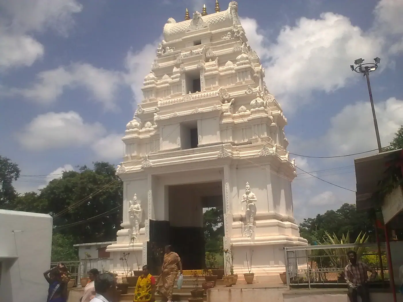 White gopuram gateway of Anantha Padmanabha Swamy Temple in Telangana, with devotees at the steps