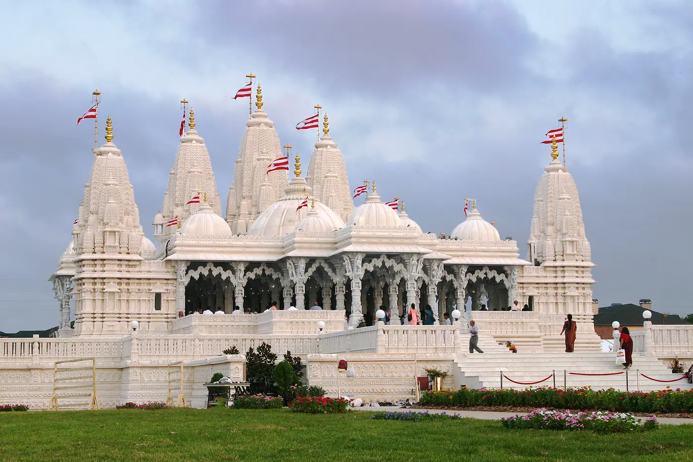 स्टैफ़र्ड, टेक्सास में सफ़ेद संगमरमर और चूना-पत्थर से बना BAPS श्री स्वामीनारायण मंदिर, नक्काशीदार शिखरों, गुंबदों और लाल-सफ़ेद ध्वजों के साथ
