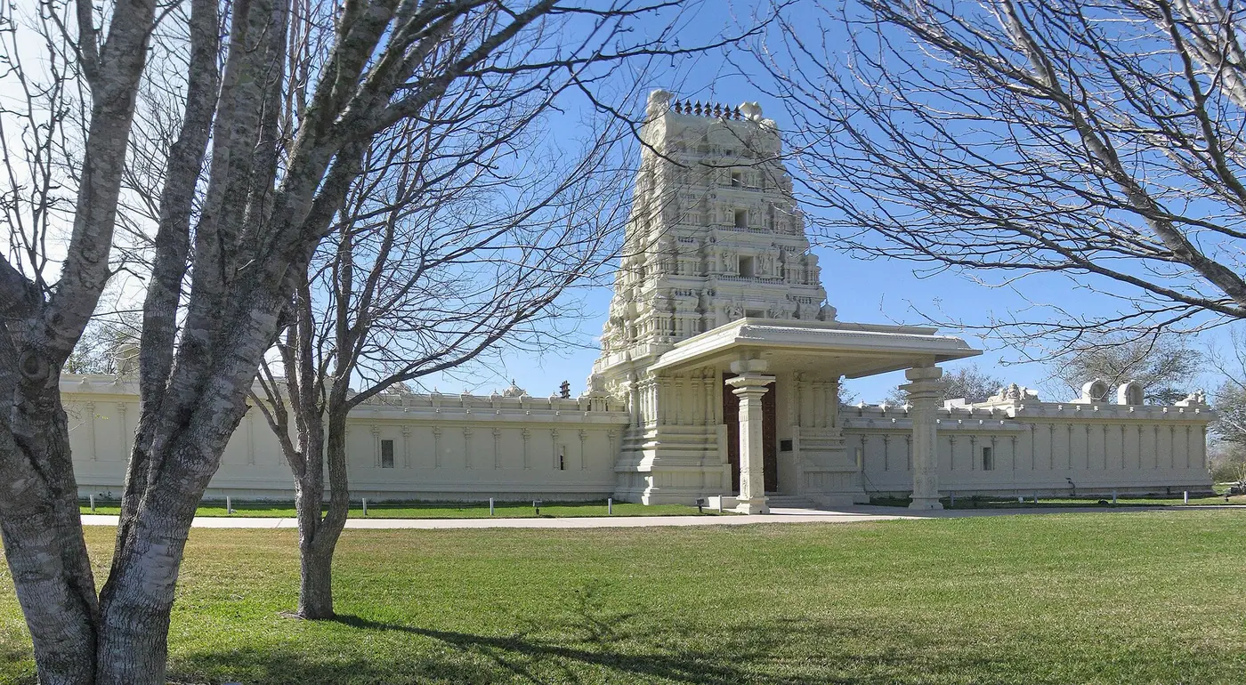 टेक्सास के पियरलैंड के पास श्री मीनाक्षी देवस्थानम् मंदिर का गोपुरम प्रवेश-द्वार और चारदीवारी, बिना पत्तों के पेड़ों के बीच से दिखती हुई