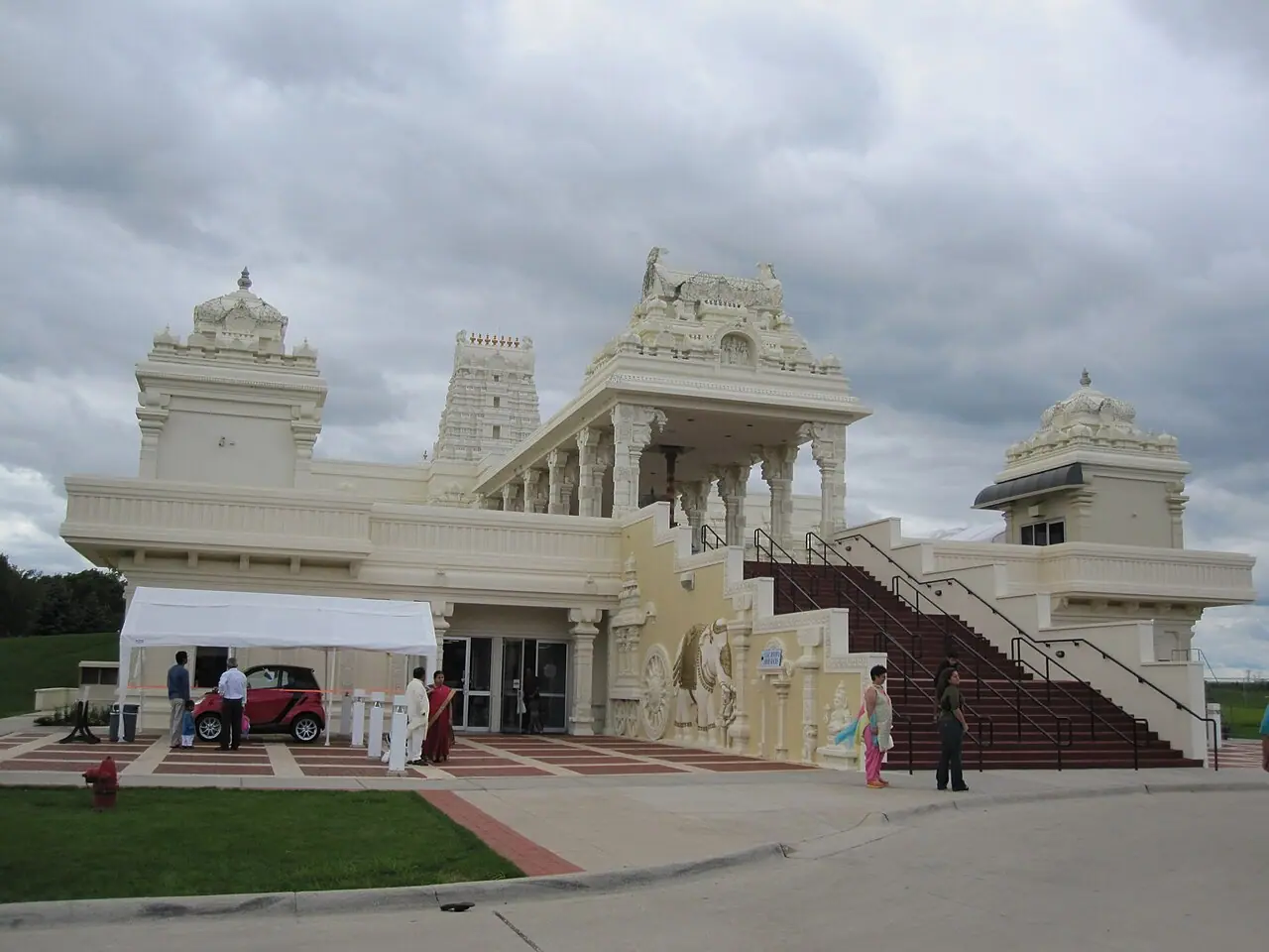 ऑरोरा, इलिनॉय स्थित श्री वेंकटेश्वर स्वामी (बालाजी) मंदिर का अग्रभाग, जिसमें बादलों भरे आकाश के नीचे क्रीम रंग का गोपुरम, प्रवेश की सीढ़ियाँ और उकेरी हुई हाथी की आकृति दिखाई देती है
